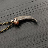 A bronze-colored canine tooth pendant necklace on a wooden surface.