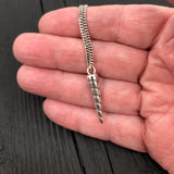 Silver necklace with a unique pendant held in a hand against a dark background